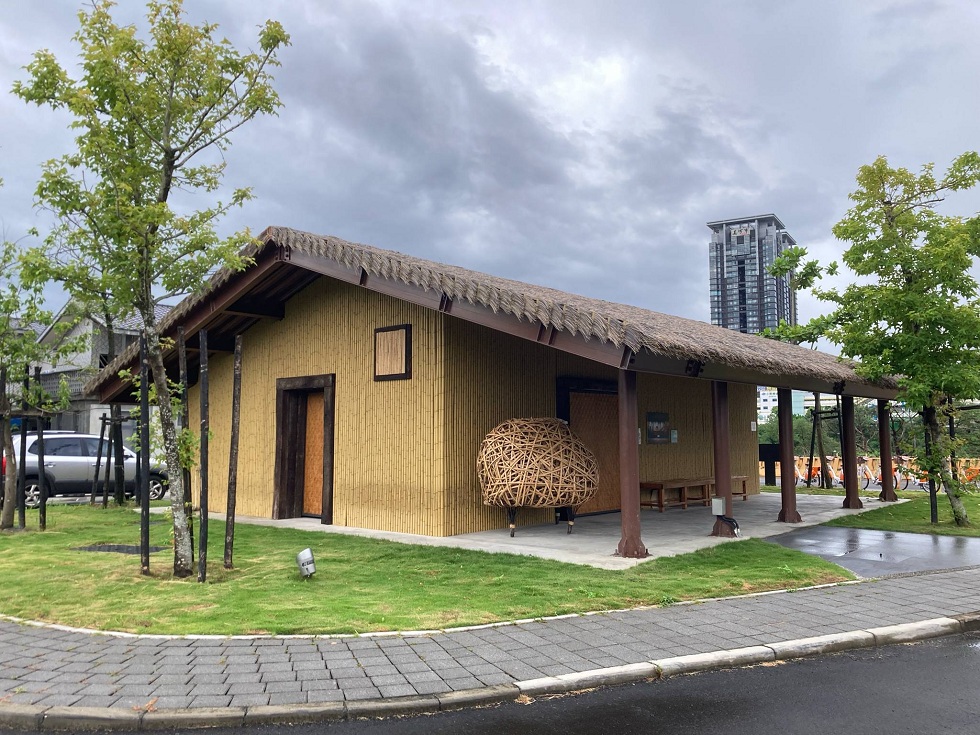 溪洲原住民族生活文化園區中新建的「傳統家屋」。後方遠處的大樓是知名建案「美河市」。