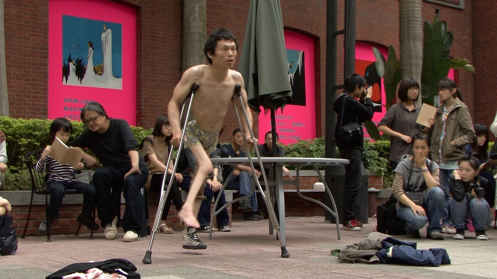 2010年阿忠的行為表演《帝國之牆》。婉玉當時尚未啟動長期拍攝，回看素材，依然能感受到阿忠的身體面對社會結構的張力與抵抗姿態。