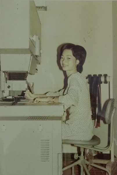 阿美在自動放相機台前處理相片，右側吊掛的是底片。