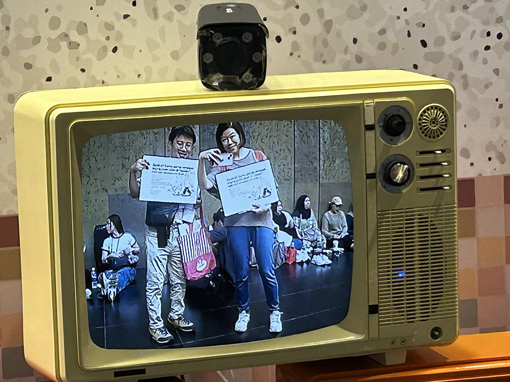 創作團隊在台北車站大廳舉著「你在台灣幫忙遛過狗嗎？」的海報徵人，路過一處影像裝置，留下了這張工作照。左為林岳德，右為貢幼穎。