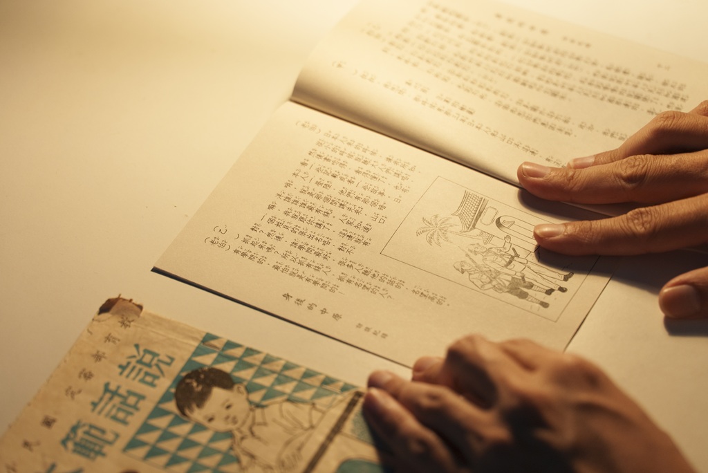 展場一隅的書桌上，擺放著與山口洋老伯的訪談文字紀錄，以及過往當地華文小學使用的《說話範本》。觀眾被安排在此經歷一段個人閱讀時光。（攝影／羅慕昕）